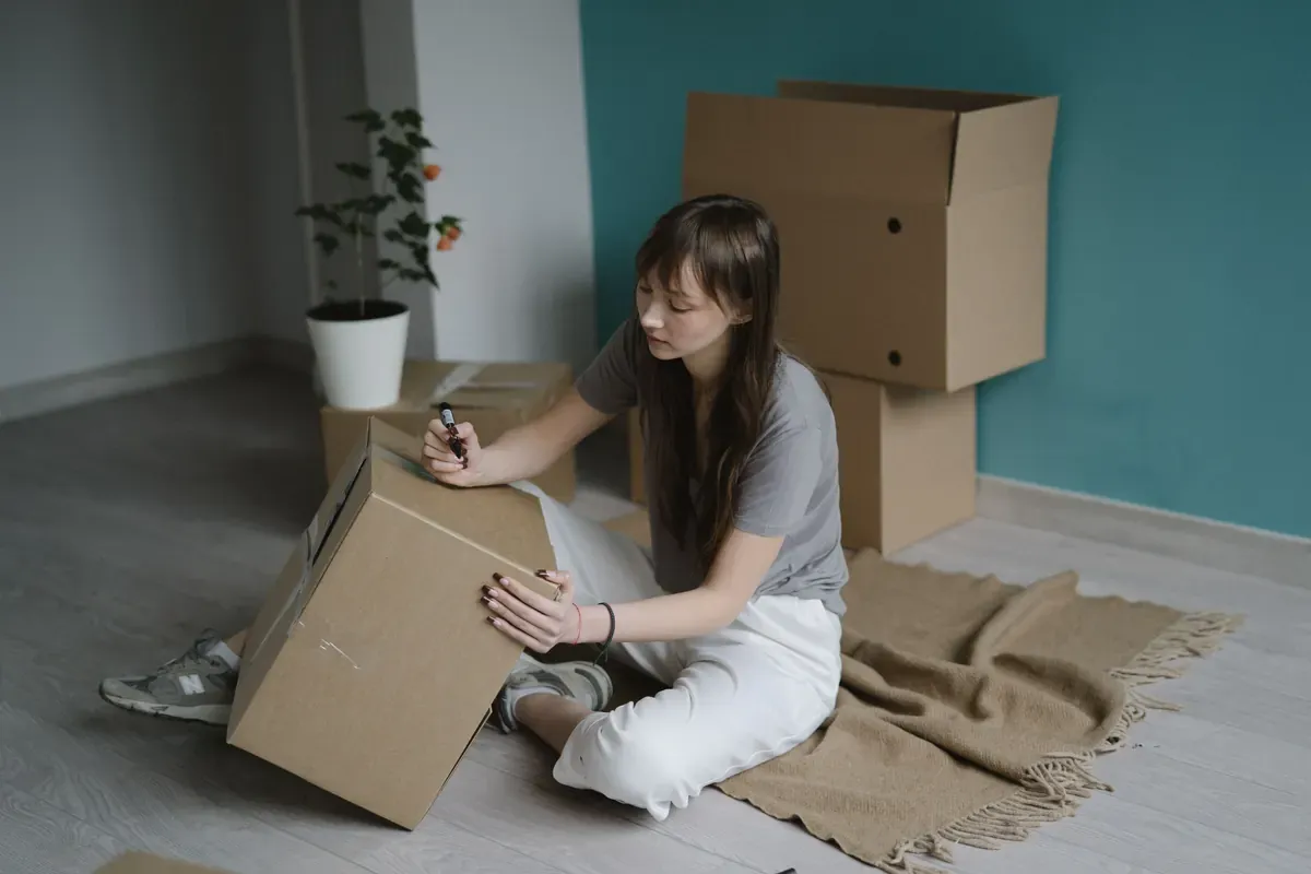A woman writes on a cardboard moving box with a marker.