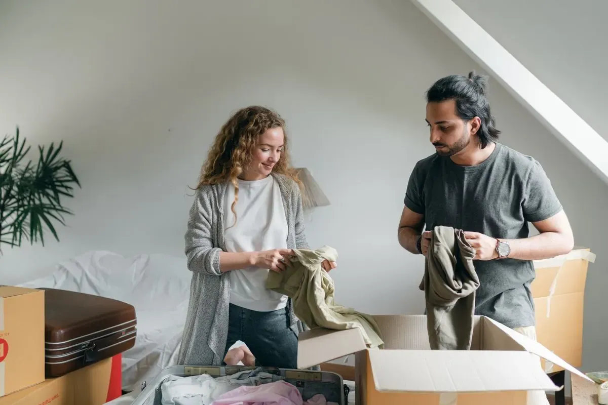 Two people sorting belongings together beside open boxes in a bedroom.