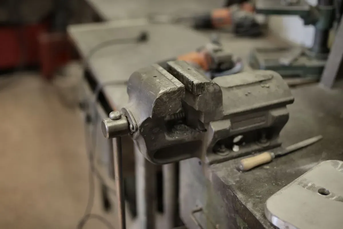 A metal vise and assorted hand tools on a well-used workshop bench.