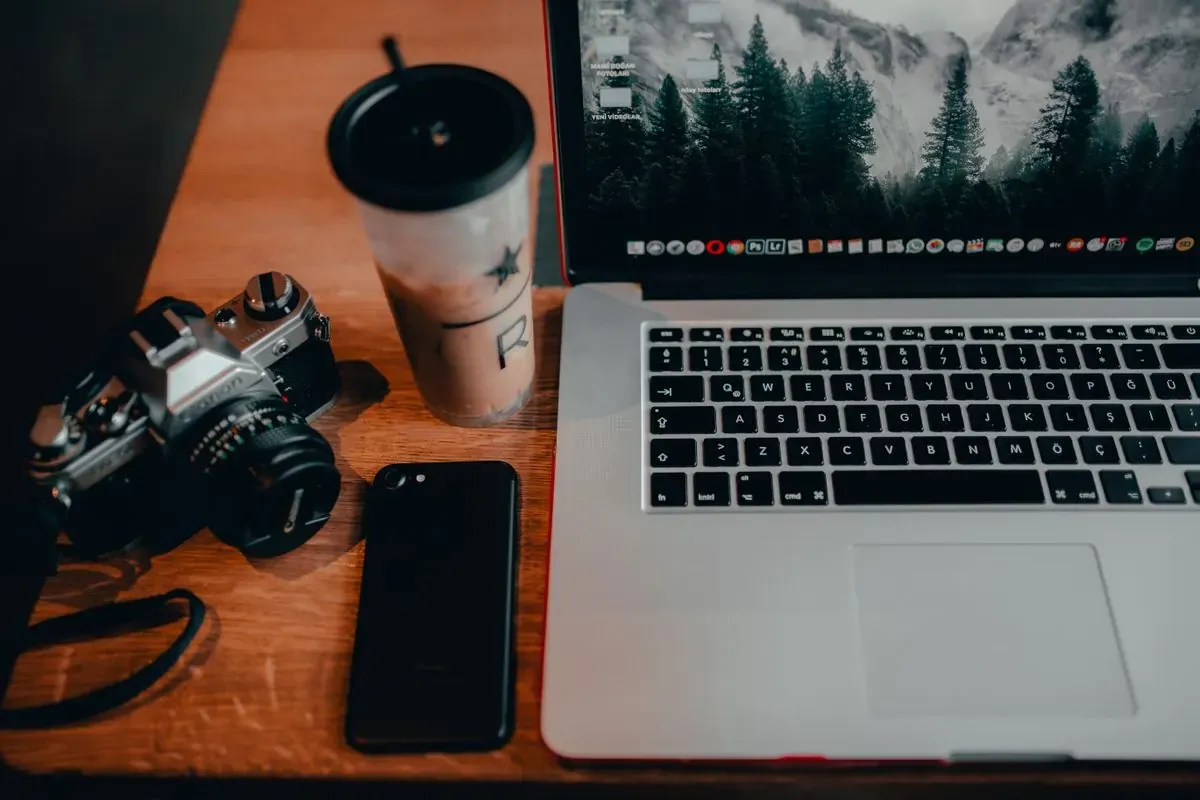 A camera, phone, and laptop arranged on a wooden table.
