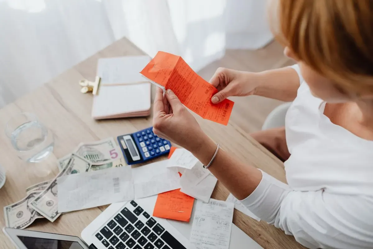 A person reviewing receipts beside a laptop, calculator, and notebook at home.