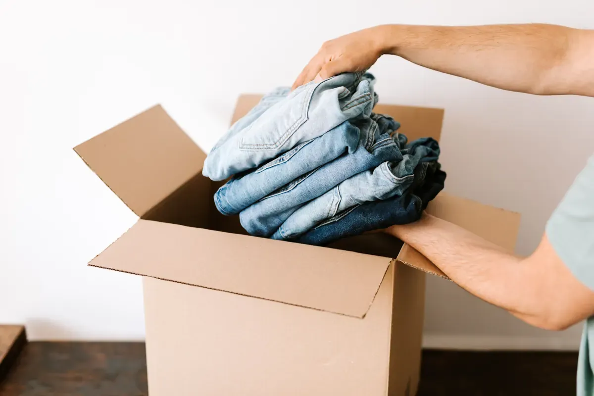A person places folded clothes into an open cardboard box.